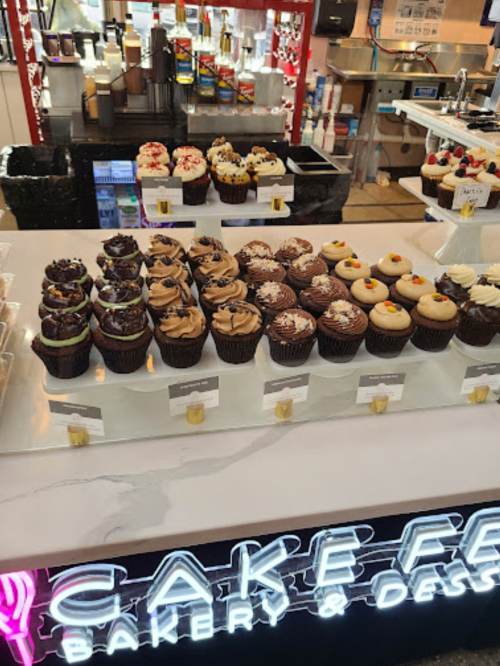 A display of assorted cupcakes in various flavors, arranged neatly on a counter at a bakery.